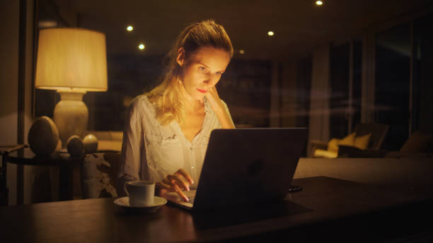 istock Businesswoman working late from home. Looking at smart phone and computer screen 1358052661