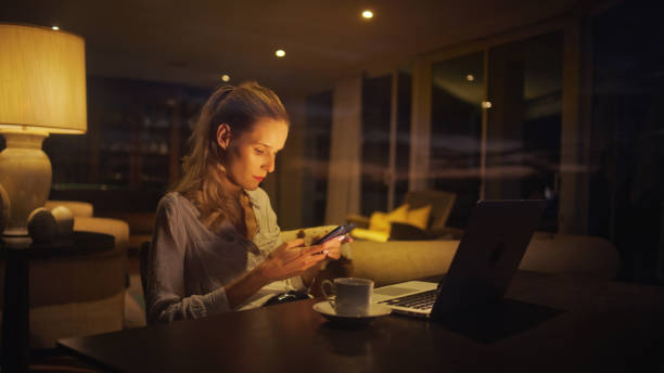 istock Businesswoman working late from home. Looking at smart phone and computer screen 1358052662