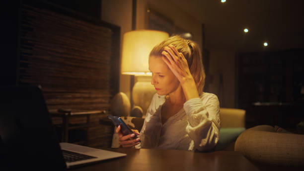 istock Businesswoman working late from home. Looking at smart phone and computer screen 1358052689