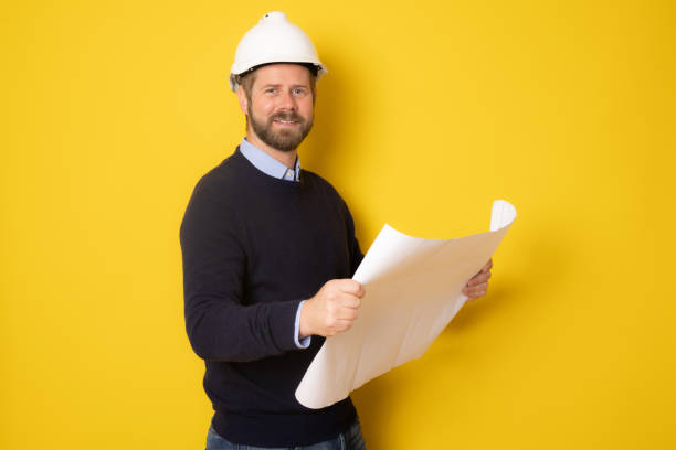 istock Young pensive architect man wearing contractor helmet holding project paper plan over isolated yellow background 1358054279