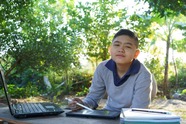 istock Boy looking at camera studying online on a wooden table with laptop computer and tablet in the morning in a rural home. concept online education countryside area and work from home 1358058858