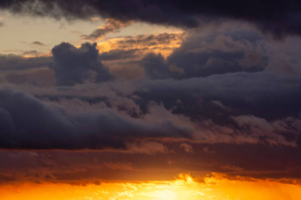 A stormy sky with dark clouds and the sunset sun breaking through the horizon