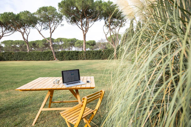 istock Table with gadgets and cup on lawn of green yard 1358061069