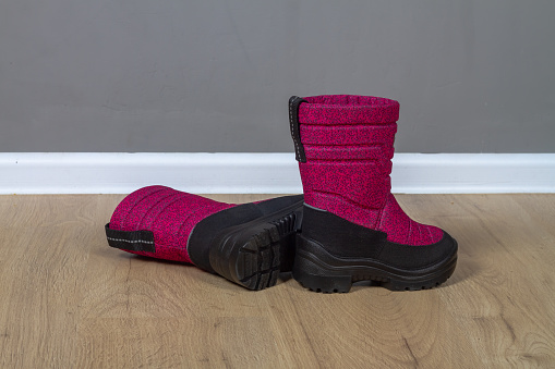 Winter boots snowboots dark pink with black soles on the floor in the room.