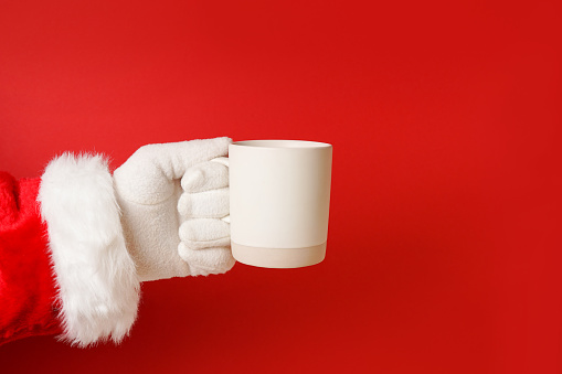 Christmas mockup Santa's hand holding white cup on red background. Christmas concept, brand