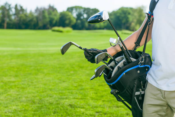 la mano del hombre en un guante de cuero negro saca un palo de golf de una bolsa. bolsa llena de palos de golf, hierro, cuña, madera, conductores. campo de césped de fondo. espacio de copia. primer plano - caddy fotografías e imágenes de stock