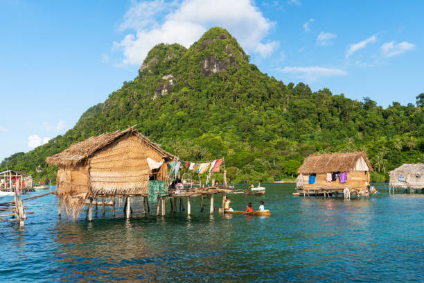 Houses made of wood and woven palm leaves in a water village against the sandstone and sedimentary rock hilltops of Tatagan Island in Semporna, Sabah, Malaysia stock photo