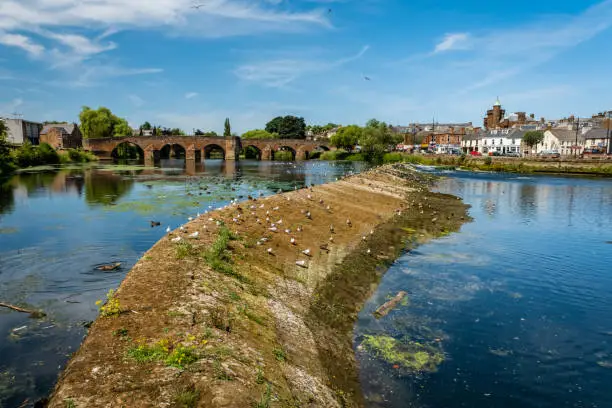 Low water and a dry caul weir during a summer drought on the River Nith in the centre of Dumfries, Scotland