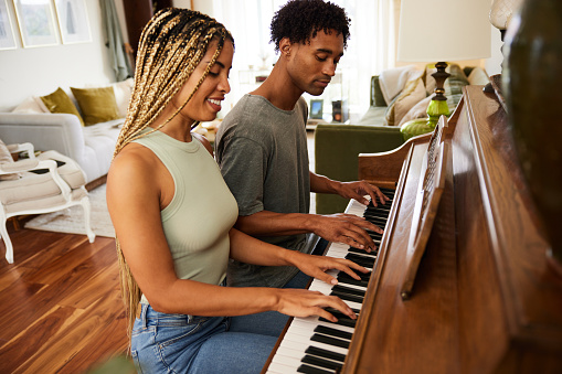 Smiling young couple playing the piano in their living room