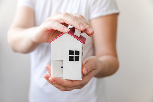 Woman hand holding toy model house isolated on white background. Real estate mortgage property insurance dream home concept. Offer of purchase rental house, family life, business real estate