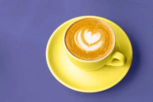Yellow cup of cappuccino with beautiful latte art on a table. Place for text. Selective focus. Color trend of the year 2022.