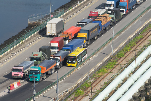 Causeway, Johor Strait - December 9, 2021: A Vaccinated Travel Lane (VTL) bus passes various trucks queued on the Johor-Singapore Causeway wait to go through a customs checkpoint, as a truck heading into Malaysia passes them in the opposite direction.