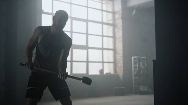 istock Angry man hitting gym tire with hammer. Guy performing physical exercises 1358083155
