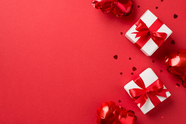 foto de la vista superior de las decoraciones del día de san valentín cajas de regalo blancas con lazos de cinta roja globos en forma de corazón y confeti sobre fondo rojo aislado con espacio vacío - valentine present fotografías e imágenes de stock