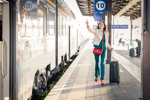 Beautiful girl running and chasing the leaving train in station. Waving hand and rushing to get on - Young business woman with suitcase running to catch the train in before it leaves the station without her