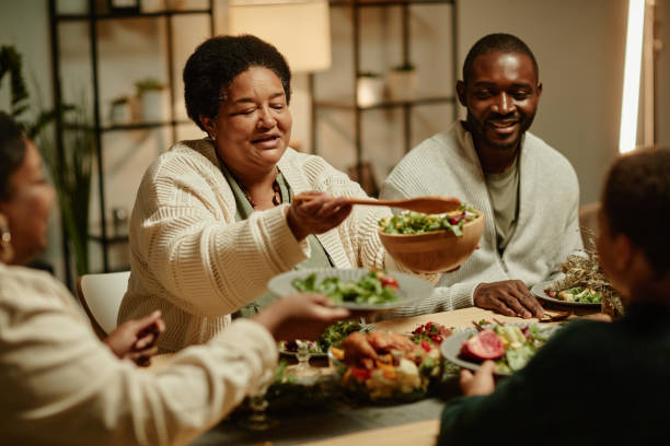 African American Grandma Serving Food at Dinner Portrait of smiling African-American grandmother serving food while celebrating Thanksgiving with big happy family at dinner table black people eating stock pictures, royalty-free photos & images