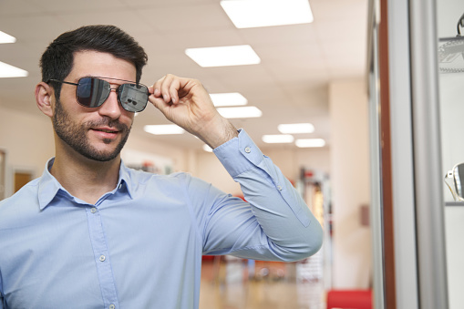 Male customer trying on mirror sunglasses and checking out his appearance while holding them by temple