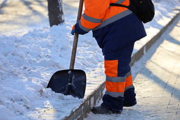 istock Worker in uniform with a shovel clears melting snow on a sidewalk 1358094394