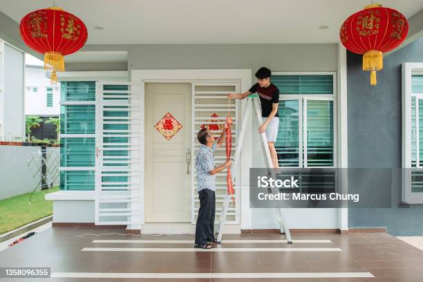 Asian Chinese Father Passing Modern Fire Crackers Lighting To Son In Front Yard Of Their House During Chinese New Years Eve Stock Photo - Download Image Now