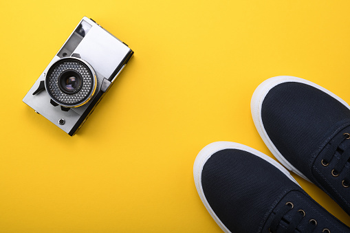 Old retro camera of the 1960s, 1970s in silver color on a yellow background with blue sneakers.