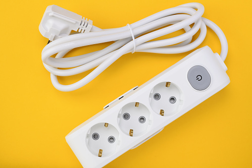White extension cord for three sockets on a yellow background. Extension cord with switch for home or office.