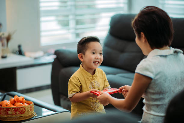 Asian chinese smiling cutie boy receiving red envelope from mother at living hall during chinese new year stock photo