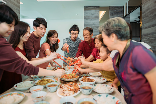 Asian chinese smiling family celebrating chinese new year's eve with raw fish salad “Yusheng” during reunion dinner