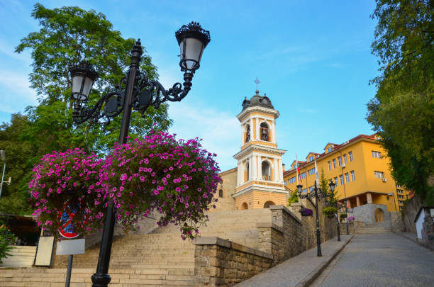 Beautiful old town with the Holy Mother of God Church in Plovdiv, Bulgaria. Purple blooming flowers, cobbled street and traditional houses. Blue sky above.
