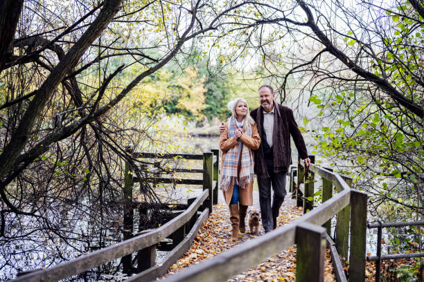 веселая пара с собакой, возвращающаяся с вида на озеро - couple autumn embracing bridge стоковые фото и изображения