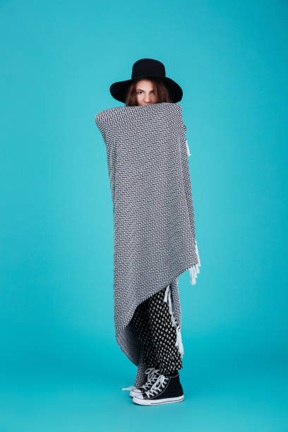 istock Young brunette woman in hat standing wrapped in blanket 1358111285