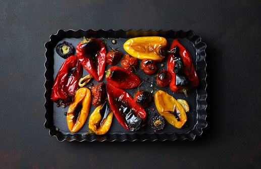 Roasted red and yellow peppers in baking tray on dark background. Directly above. Vegetables food.