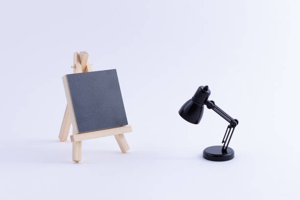 istock Wooden Easel Miniature with Blank Black Square Canvas and Table Lamp 1358113290