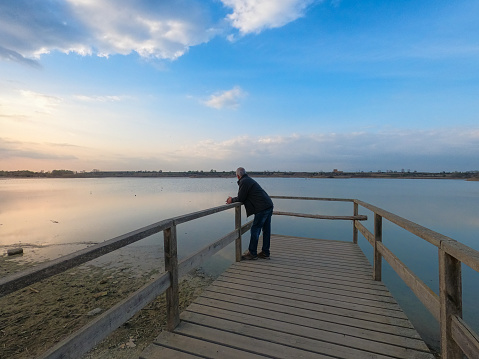 Older man watching the sunset on the lake pier on a winter day. Beautiful scenery of Lake Ibars Vilasana in Catalonia, northern Spain. Sunset on the lake