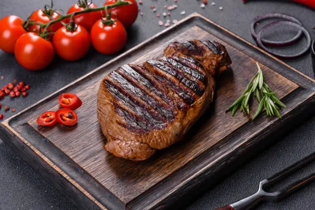 Cooked grilled Chuck eye roll steak on a chopping Board. Dark background