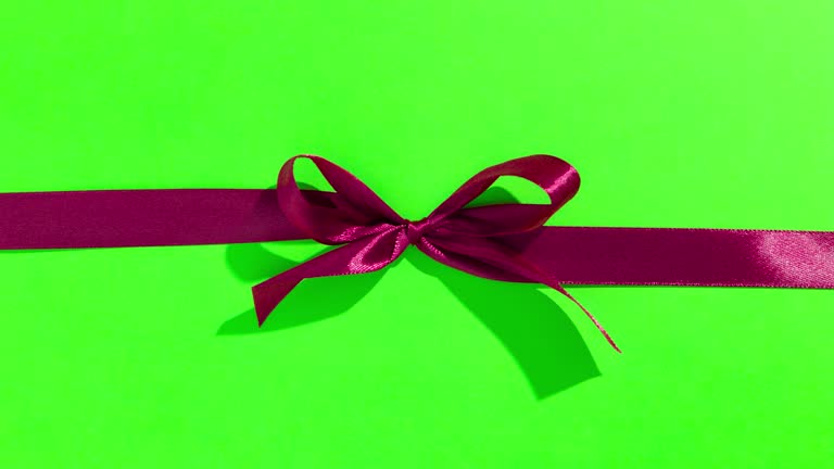 Red ribbon with bow on green screen, opening and unpacking a gift, top view - Stop motion animation for Valentine's Day, Christmas.