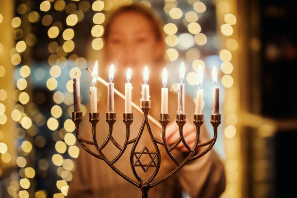 Girl Lighting Menorah For Hanukkah An elementary age child lighting the Menorah candles with a long match for Hanukkah celebration over the holiday. candlestick holder photos stock pictures, royalty-free photos & images