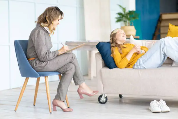 Joyful teen girl eats on couch during psychotherapy. Teenage psychologist.