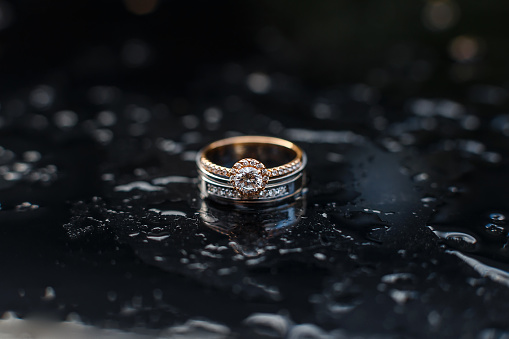 Elegant wedding diamond rings laying among raindrops . Expensive engagement rings with gem stones. Wedding jewellery accessories. Macro photo with soft selective focus