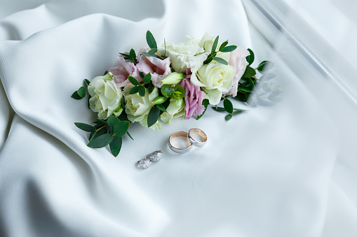 Wedding rings and earrings from white gold with gemstones lying near gentle hairpin from flowers and shining. Bridal jewelry and accessories close-up