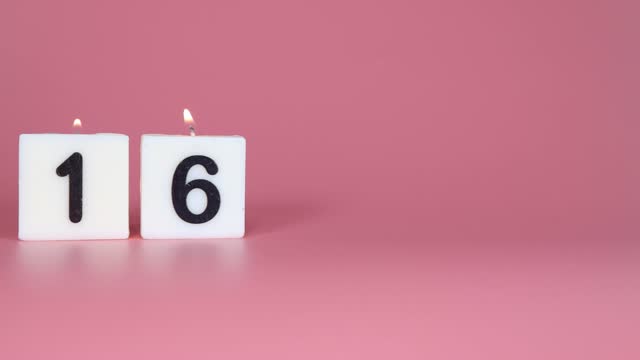 A square candle saying the number 16 being lit and blown out on a pink background celebrating a birthday or anniversary
