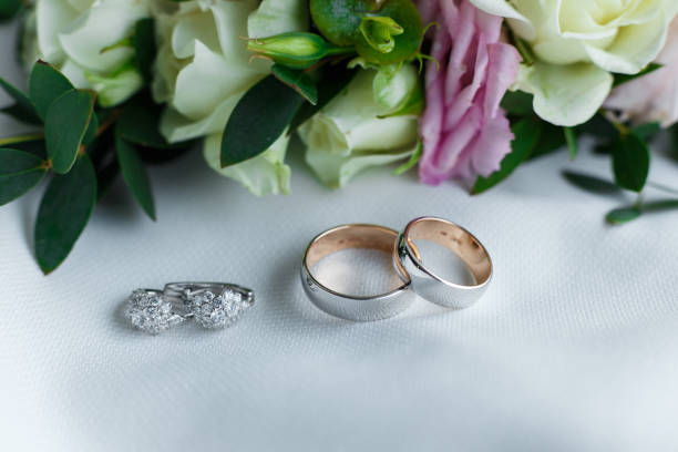 花から穏やかなヘアピンの近くに横たわり、輝く宝石とホワイトゴールドからの結婚指輪やイヤリング。ブライダルジュエリーとアクセサリークローズアップ - pair ストックフォトと画像