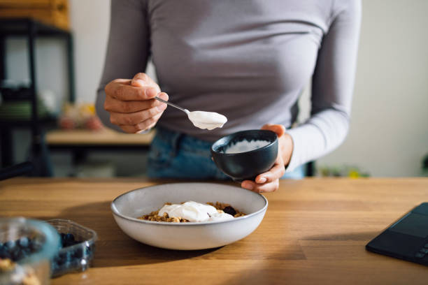 Close Up of Woman Hands Making Healthy Breakfast in Kitchen An anonymous Asian woman mixing cereals, greek yogurt and blueberries in a bowl on a kitchen table at home. yoghurt stock pictures, royalty-free photos & images