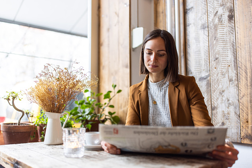 Businesswoman reading newspaper in cafe, Young female sitting at coffee shop table reading a newspaper.