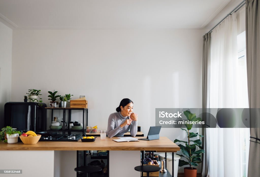 Happy Business Woman Working from Home Beautiful Asian businesswoman using digital tablet at kitchen desk. Working At Home Stock Photo