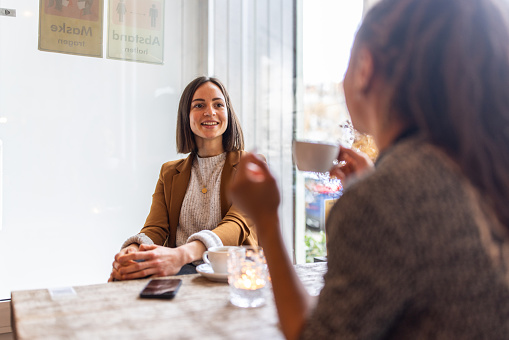 Young businesswoman meeting with a female colleague at coffee shop. Two business women talking while having a coffee at a cafe.