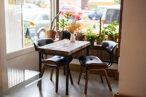 Empty modern cafe interior with chairs and table near a window with potted plants. Empty table at a restaurant.