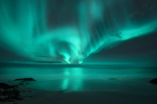 Aurora boreal sobre el mar. Auroras boreales en las islas Lofoten, Noruega. Cielo estrellado con luces polares. Paisaje nocturno con aurora, mar con agua borrosa y reflejo del cielo, playa de arena. Aurora photo