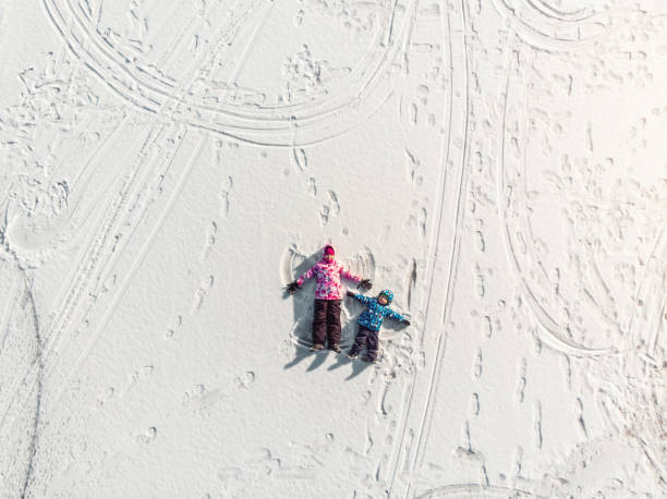 Aerial top view pair two cute little sibling kids boy girl have fun play make snow angel on white frozen lake ice surface landscape bright sunny cold season day. Outdoor family winter activity Aerial top view pair two cute little sibling kids boy girl have fun play make snow angel on white frozen lake ice surface landscape bright sunny cold season day. Outdoor family winter activity. top of ski mountain stock pictures, royalty-free photos & images