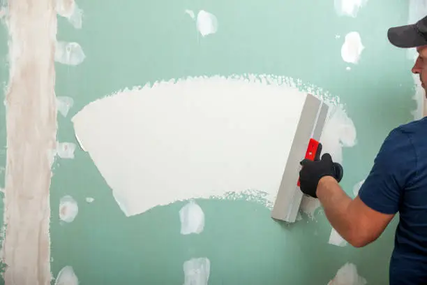 Hand with a spatula. Worker trowels putty on drywall with finishing putty