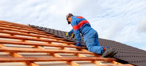 Man worker uses a power drill to attach a cap  metal roofing job with screws.